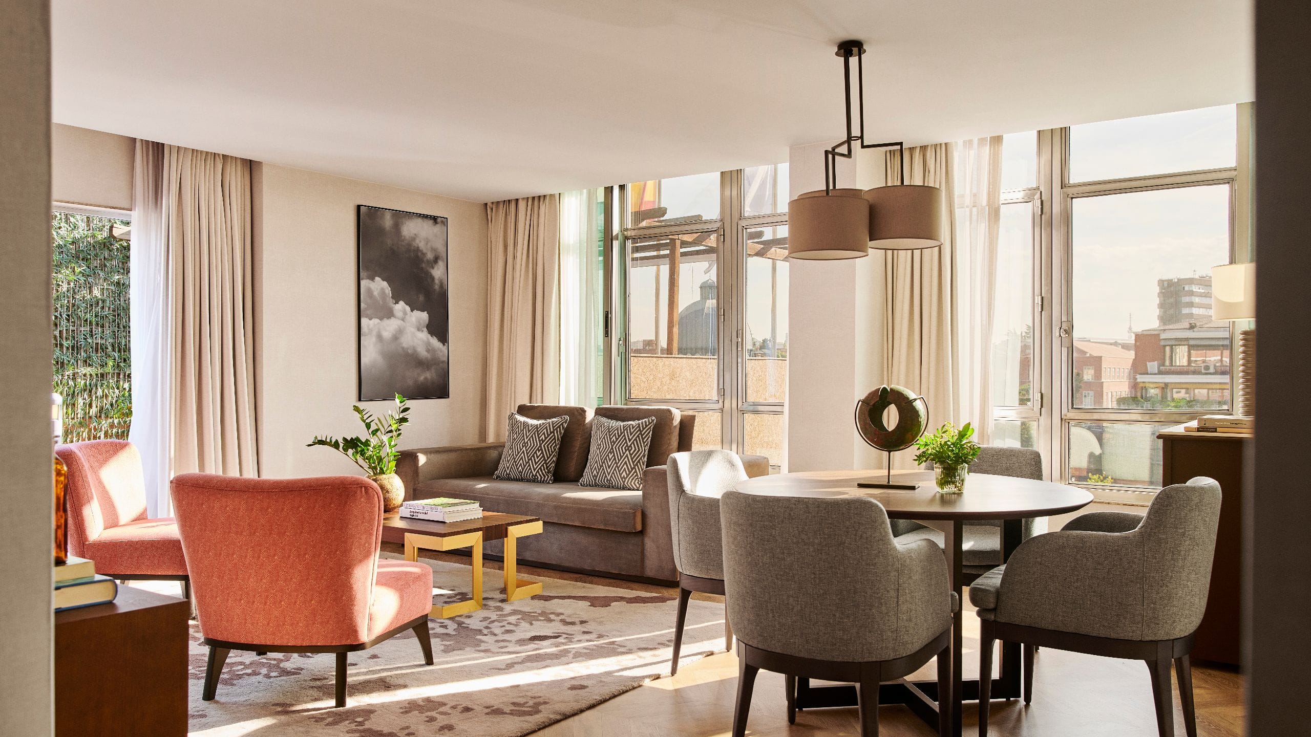 Suite living room with a sofa, coral armchairs and a round dining table beside floor-to-ceiling windows.