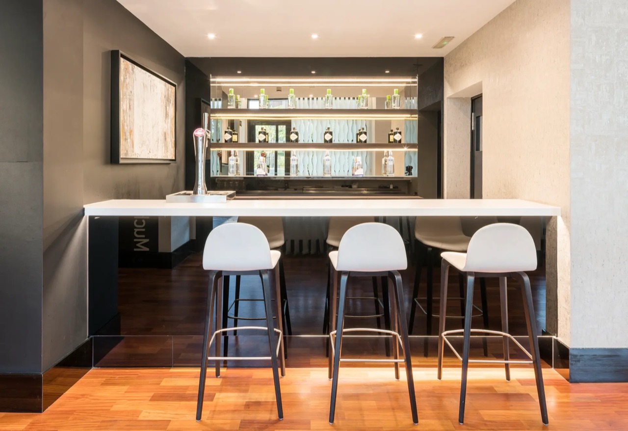 A bar counter with stools, a beer tap, and shelves of spirit bottles reflected in a mirrored backsplash.