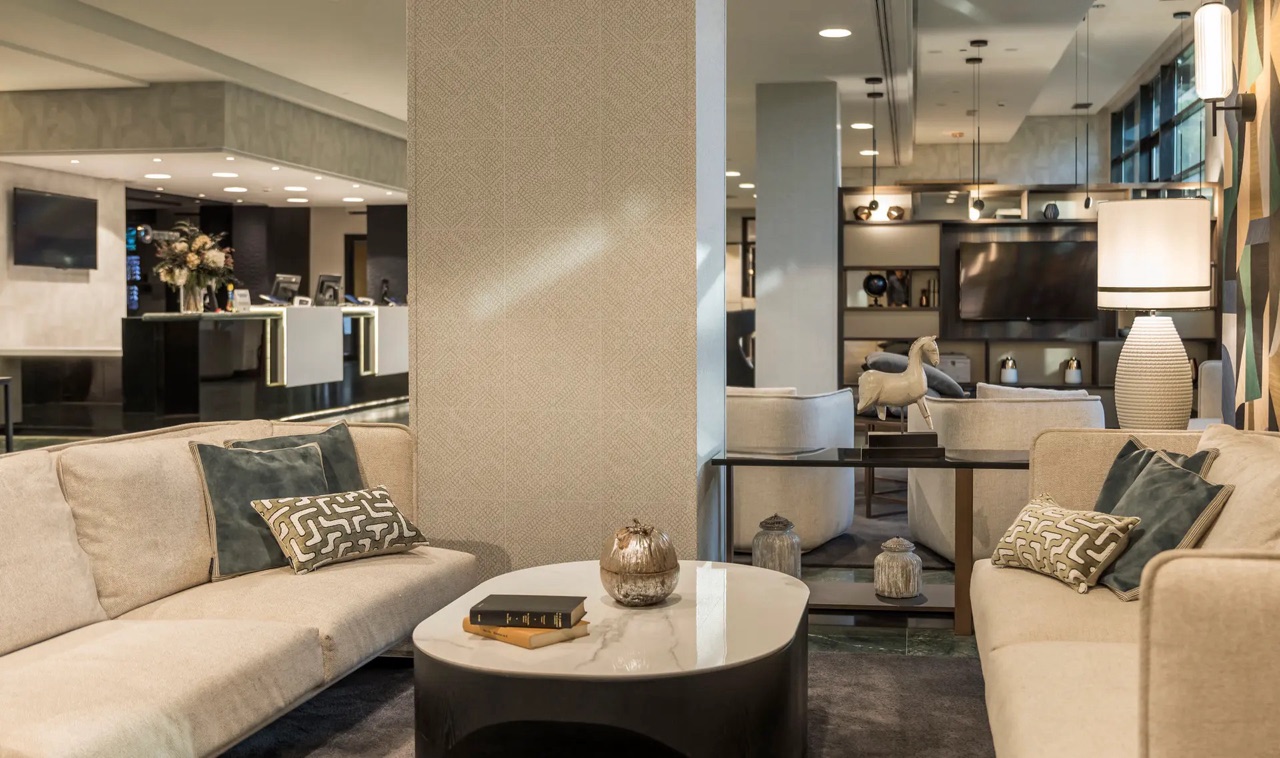 A lobby seating area with beige sofas and a marble coffee table, with the front desk visible in the background.