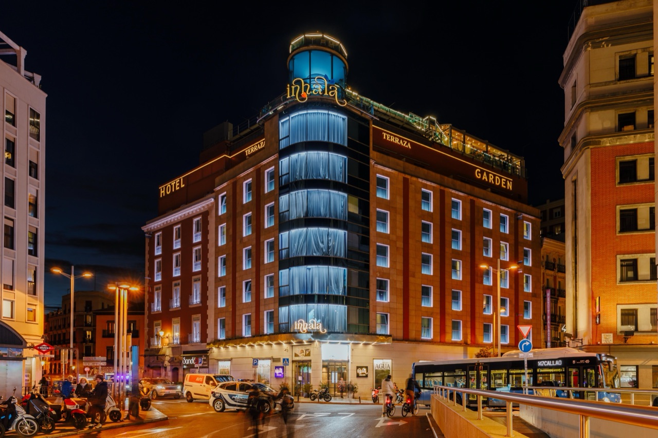 The lit-up red brick facade of Inhala Hotel Garden at night, with the Inhala and Garden signage on the building and a rounded glass tower.