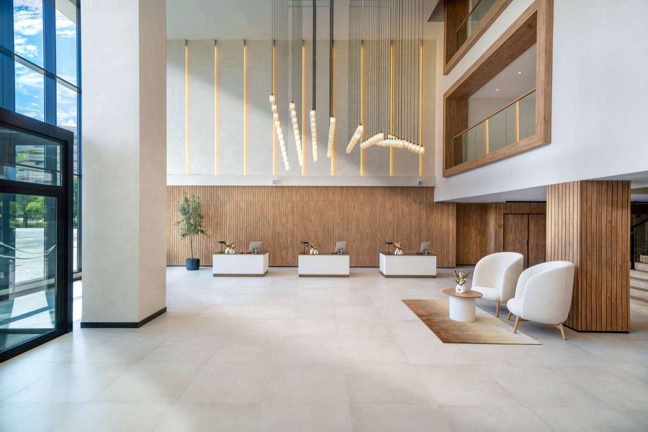 The hotel lobby with a double-height wood-panelled reception wall, hanging pendant lights, three check-in desks and a seating area.
