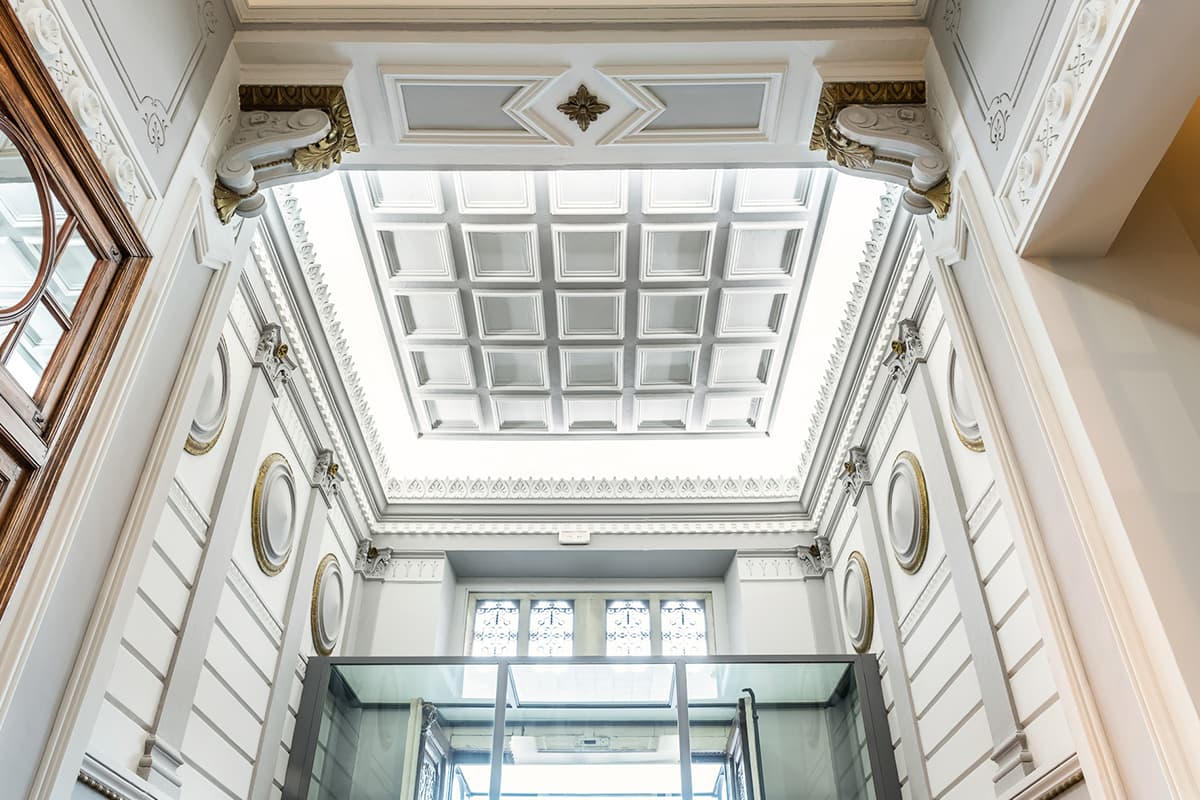 A coffered skylight ceiling above the hotel's entrance hall, seen from below with a glass elevator shaft in the foreground.