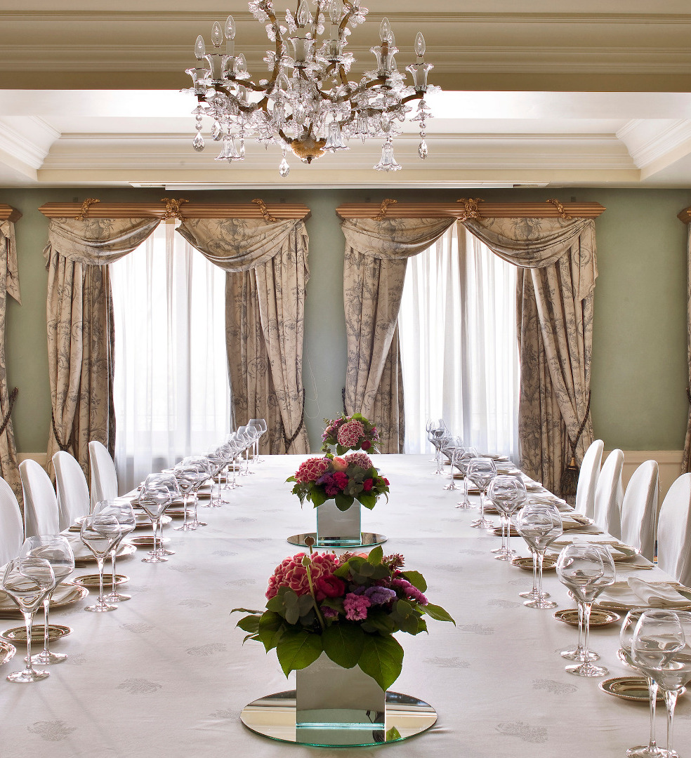 A private dining room with a long white-clothed table set with wine glasses and floral centrepieces beneath a crystal chandelier.