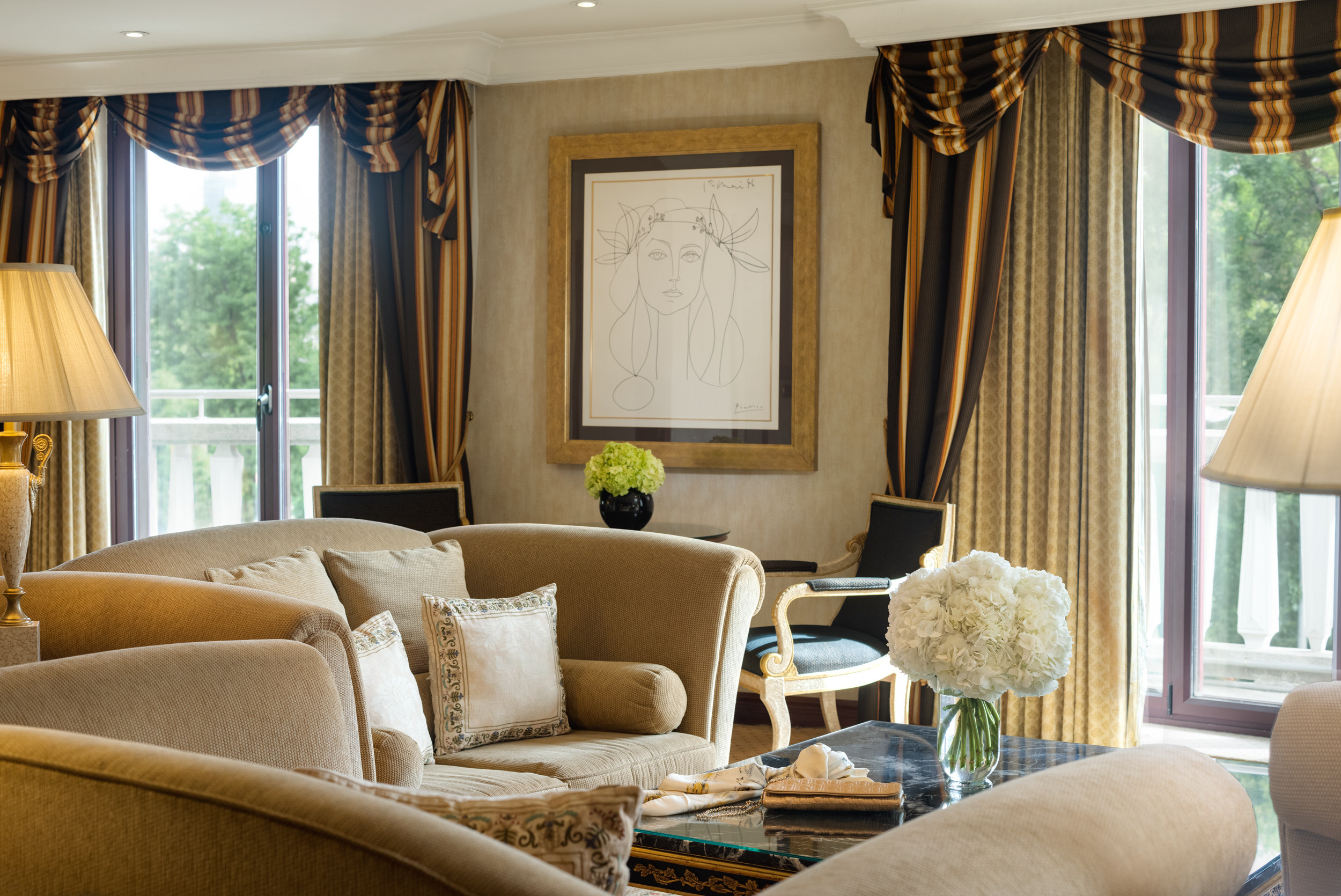 A suite sitting room at InterContinental Madrid, with tall balcony windows, framed artwork and upholstered sofas.
