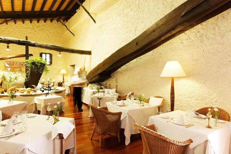 Restaurant dining room in the former olive mill, with exposed wood beams, stone walls and wicker chairs