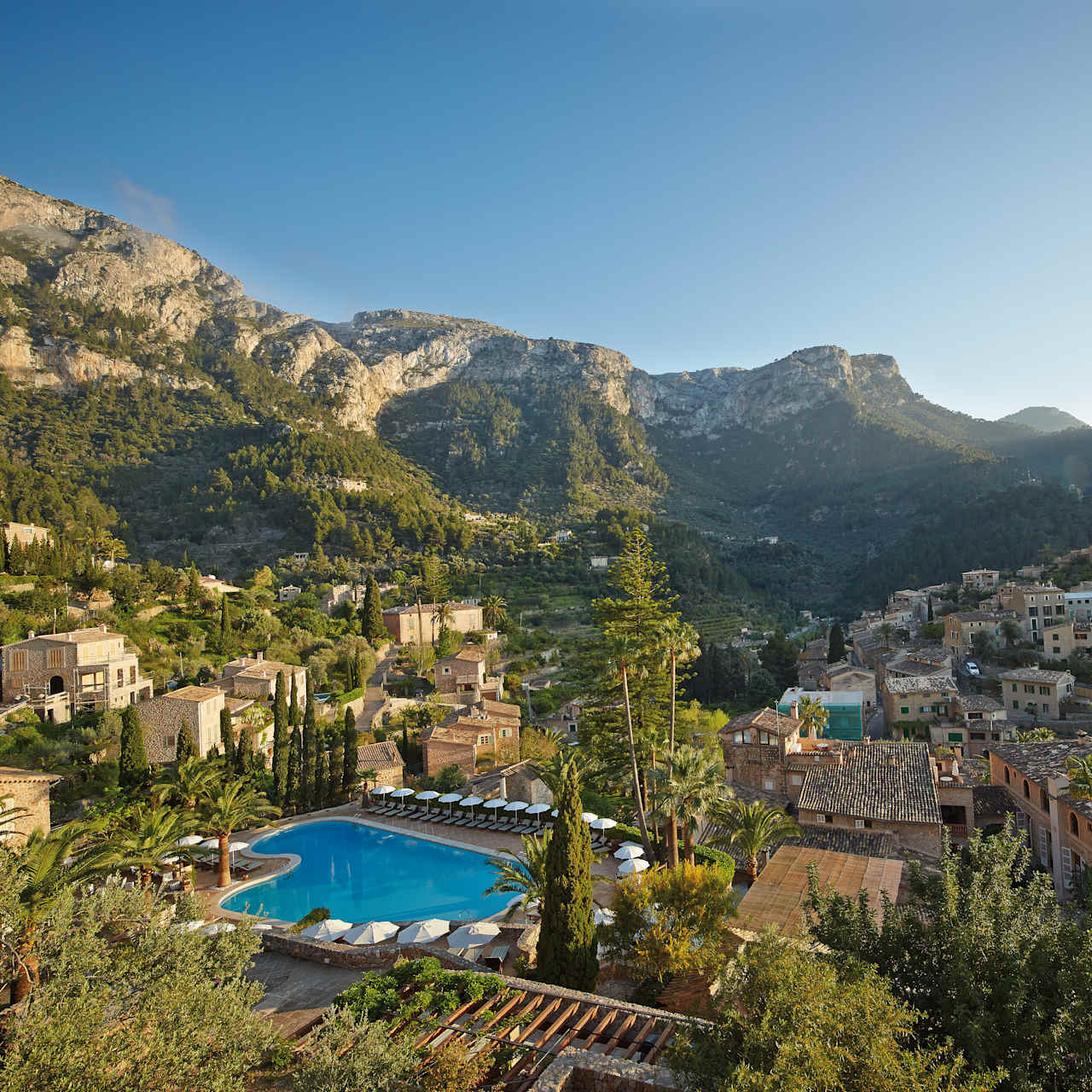 Aerial view of La Residencia's stone buildings, pool, and surrounding Deia village and mountains
