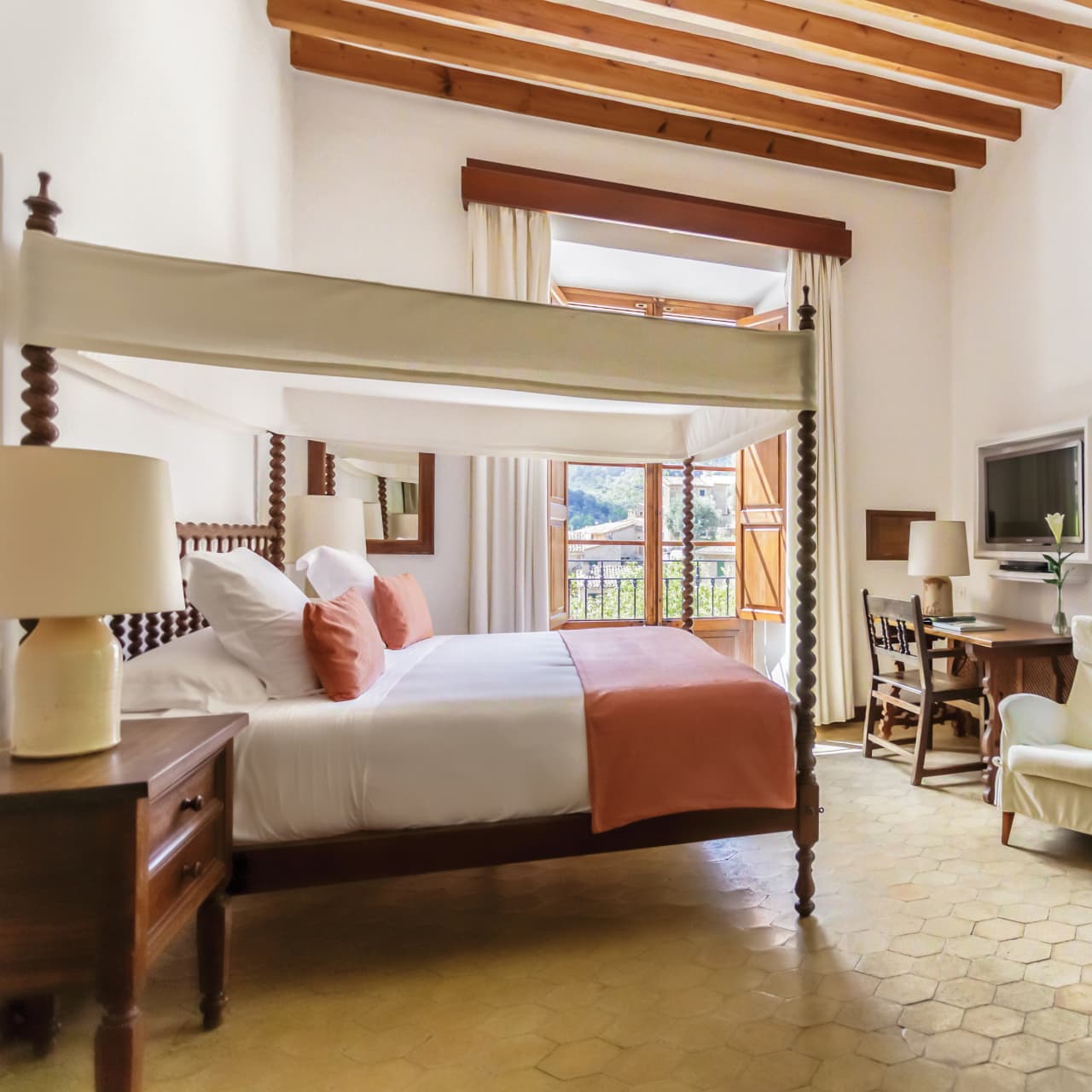 Deluxe double room at La Residencia with a four poster canopy bed, wood beam ceiling, and a balcony over the village
