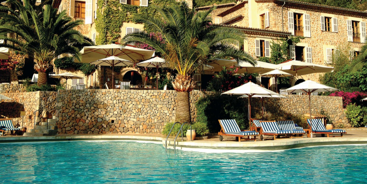 Poolside terrace at La Residencia with sun loungers, umbrellas, and the stone manor house facade behind