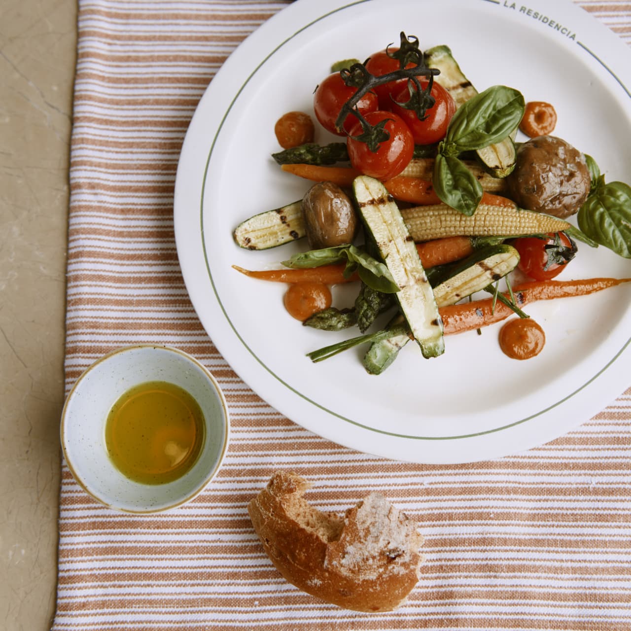 Grilled vegetable dish served on a La Residencia branded plate with bread and olive oil on the side