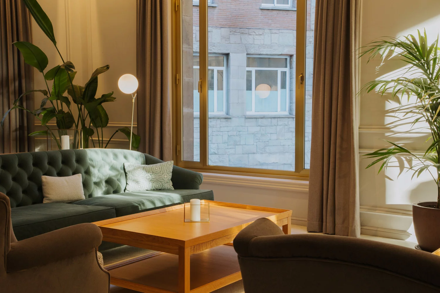 Lounge with a green tufted sofa, armchairs and a wooden coffee table by a window