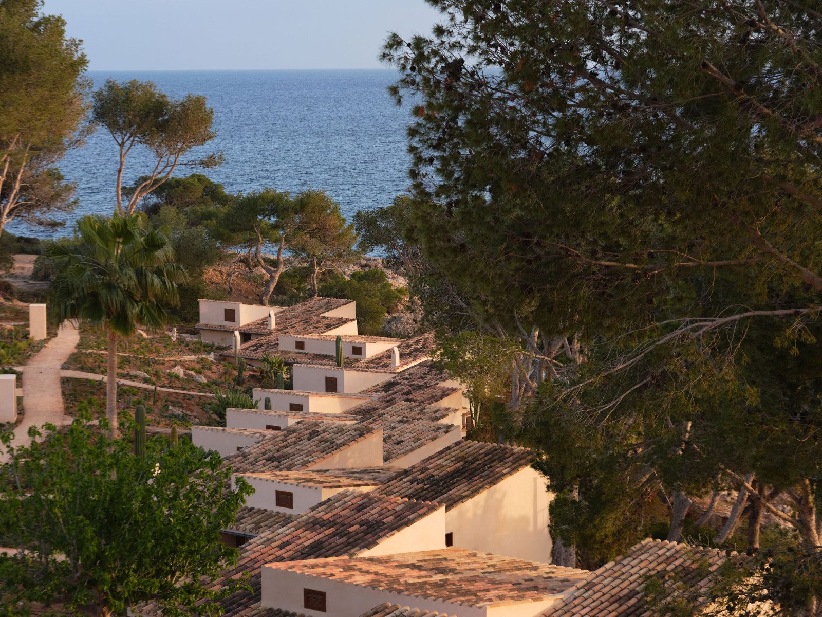 Hillside casitas with traditional Mediterranean tiled roofs at Mandarin Oriental Punta Negra, Mallorca, set among pines with the sea visible below