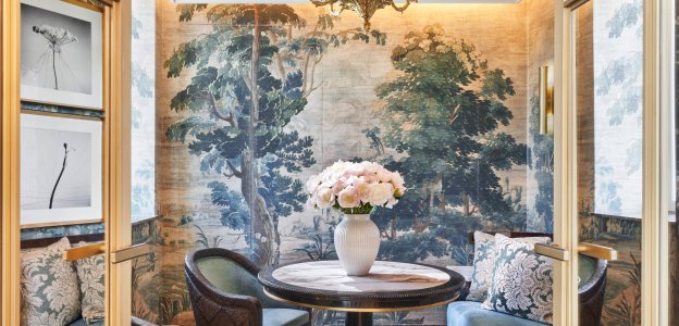 An alcove with a curved banquette and two armchairs around a marble-topped round table, its walls covered in a painted forest mural.