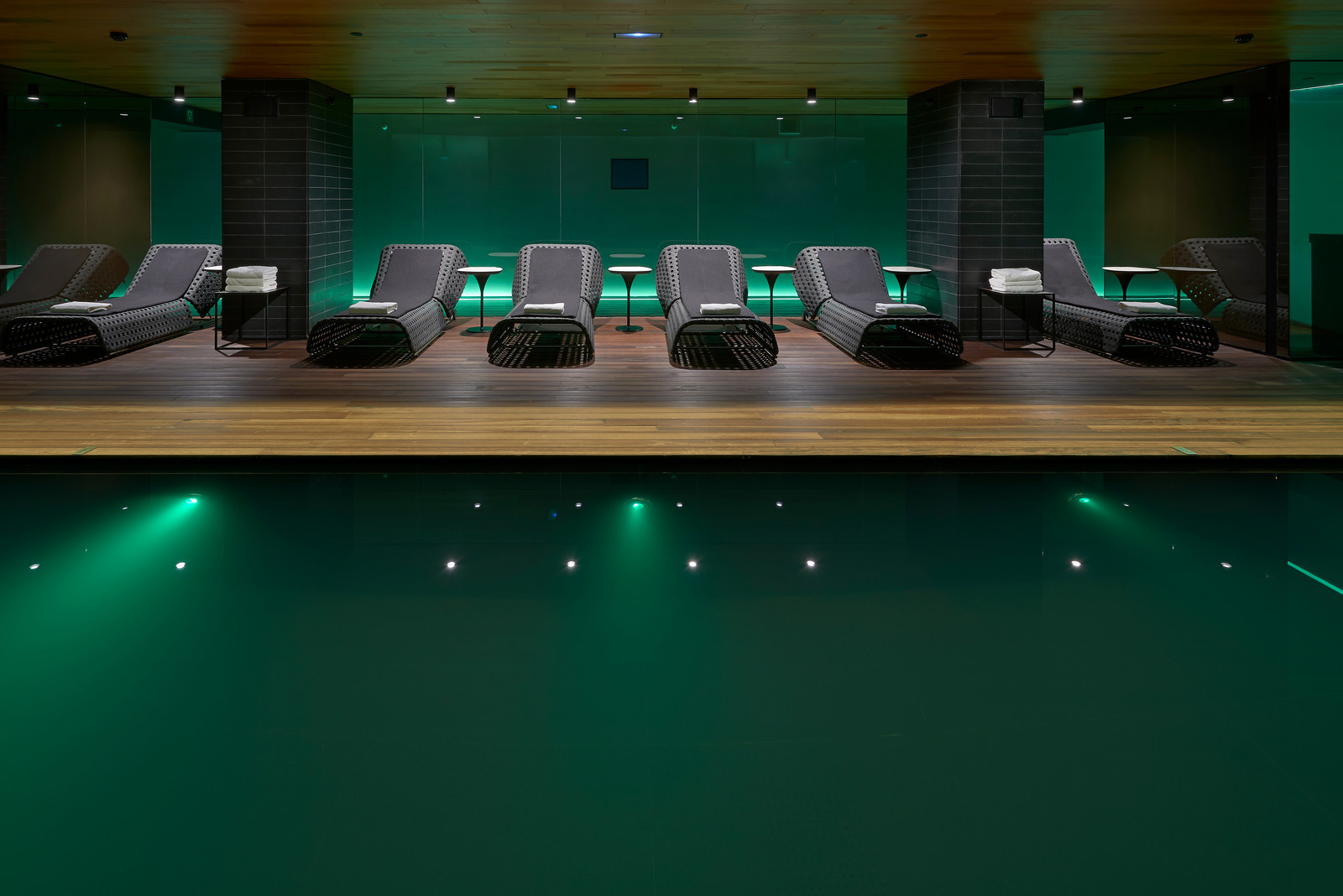 Indoor spa pool with loungers lit by green ambient lighting