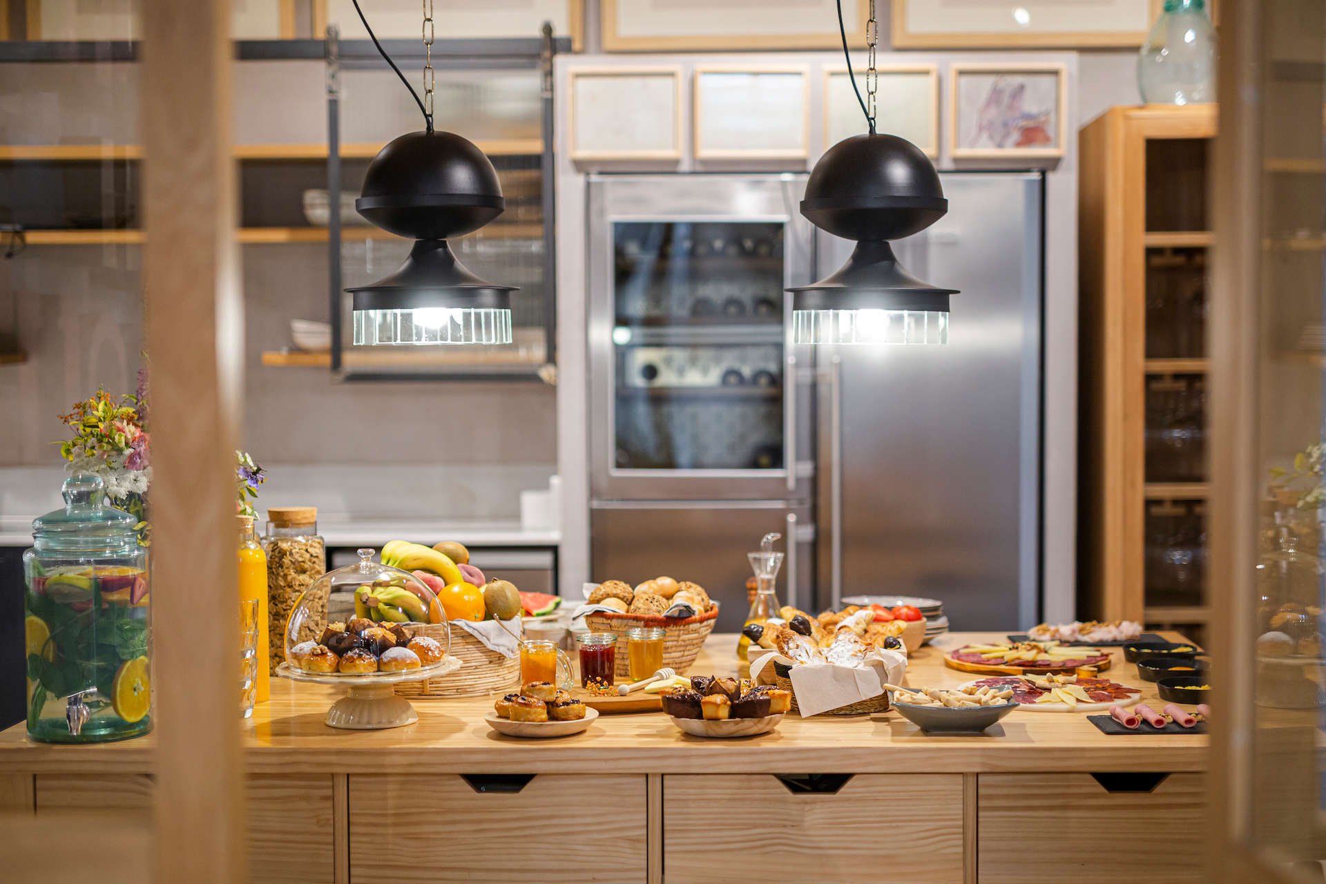 Breakfast spread in the open kitchen of the dining room at Margot House, with fruit, juices and pastries under black pendant lamps