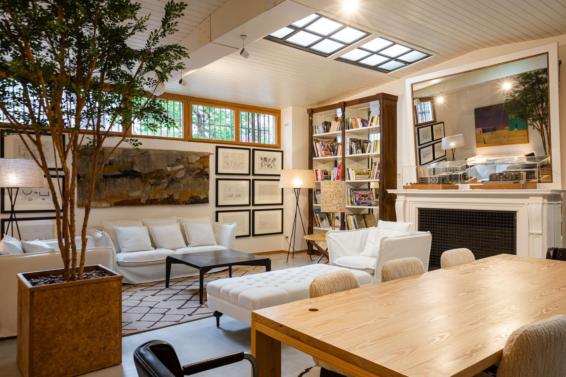 Library corner of the salon at Margot House with white sofas, a fireplace, bookshelves and a wooden table