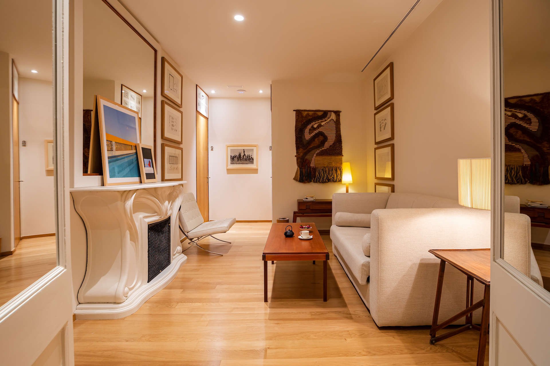 Sitting area of a room at Margot House with a white marble fireplace, a cream sofa, a wooden floor and framed art