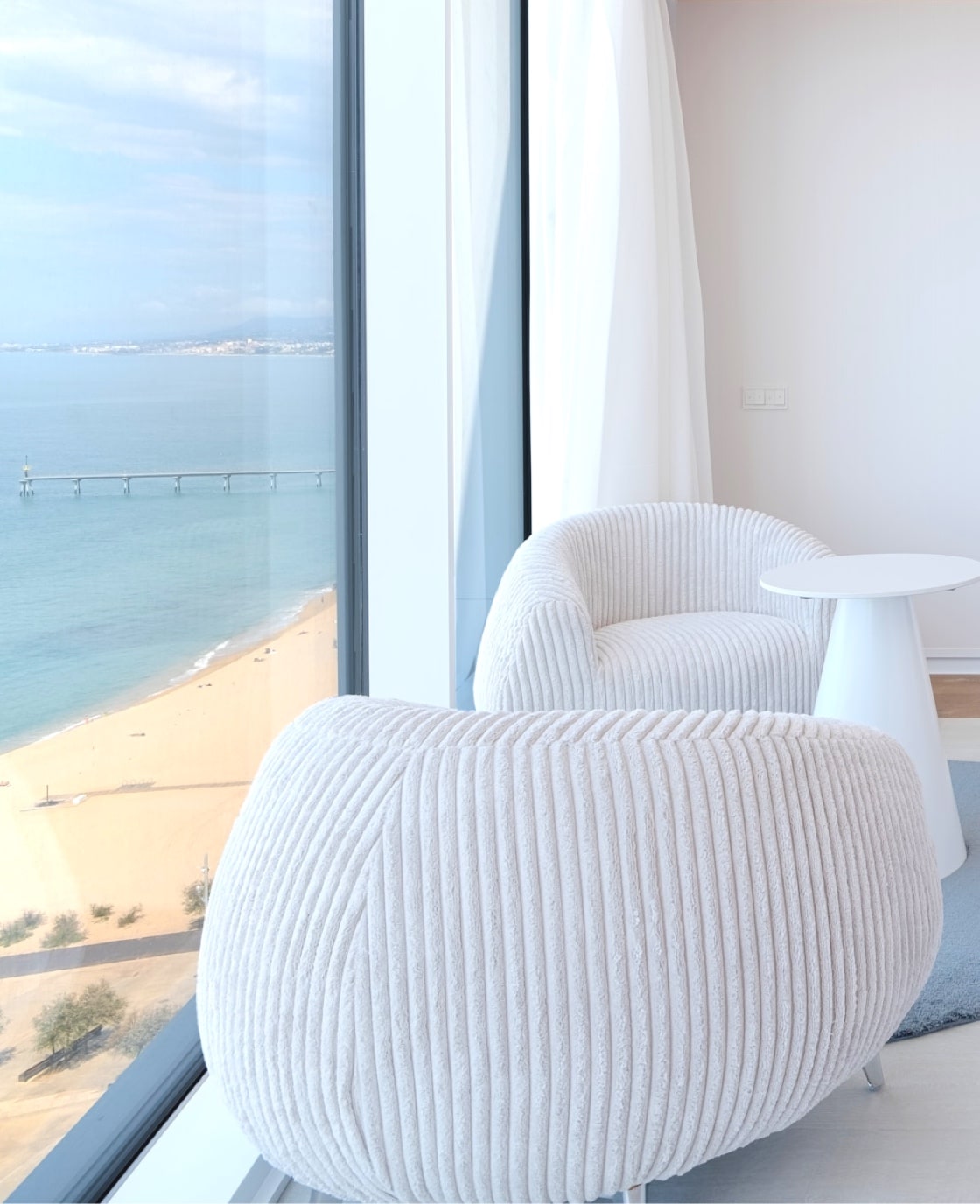 Guest room armchairs beside a floor-to-ceiling window with a beach and sea view