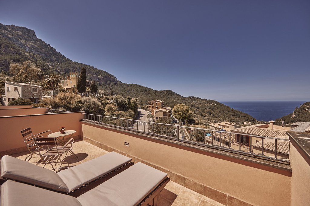 Private room terrace with a table, chairs and sun loungers, overlooking the village of Estellencs, the Tramuntana mountains and the sea.