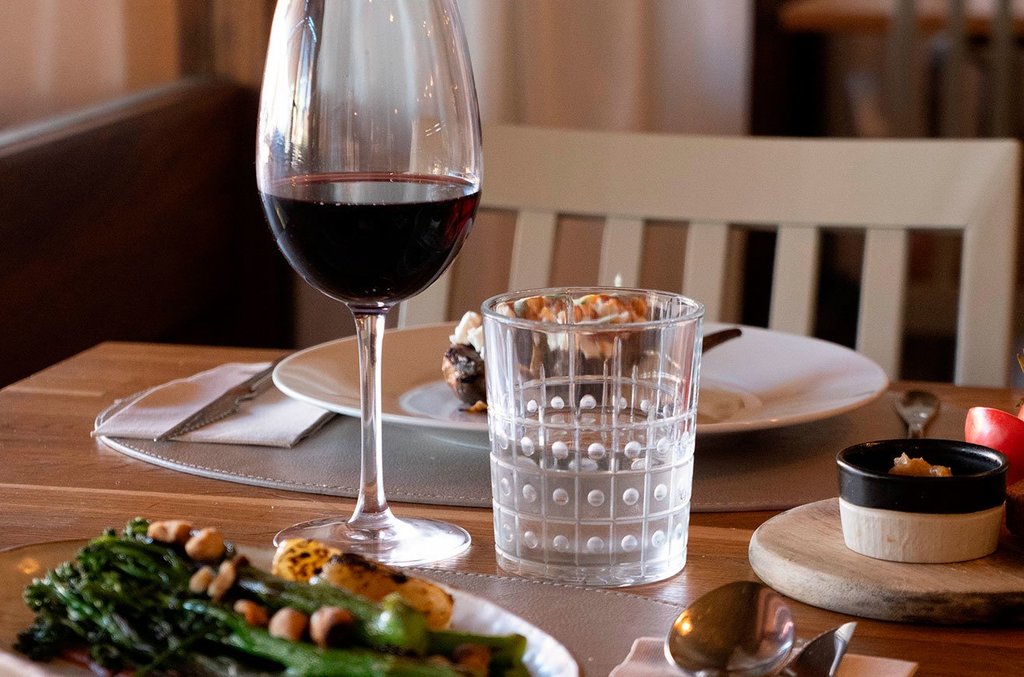 Restaurant table set with a glass of red wine, a plated dessert, and a dish of green vegetables with nuts.