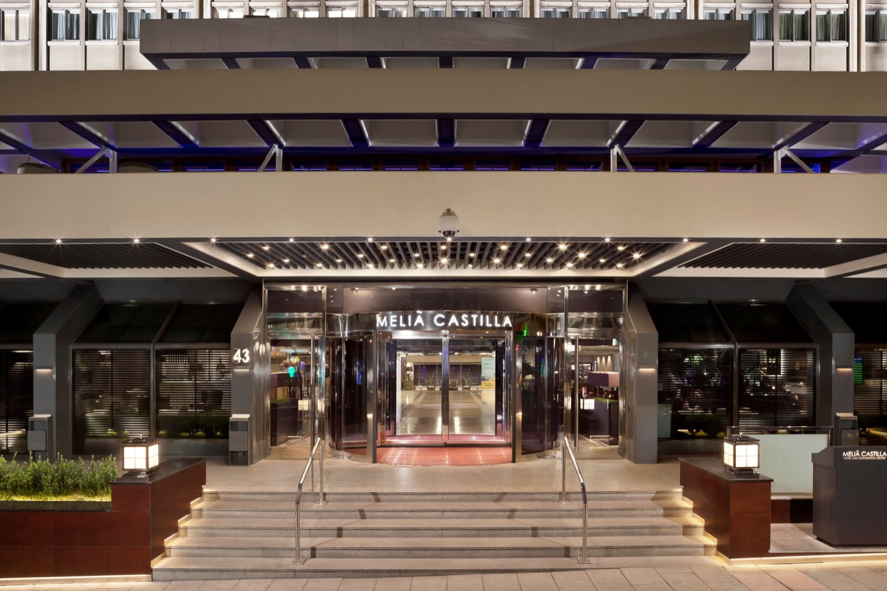 Meliá Castilla's illuminated entrance canopy and revolving door at night, with the hotel name lit above the doors.