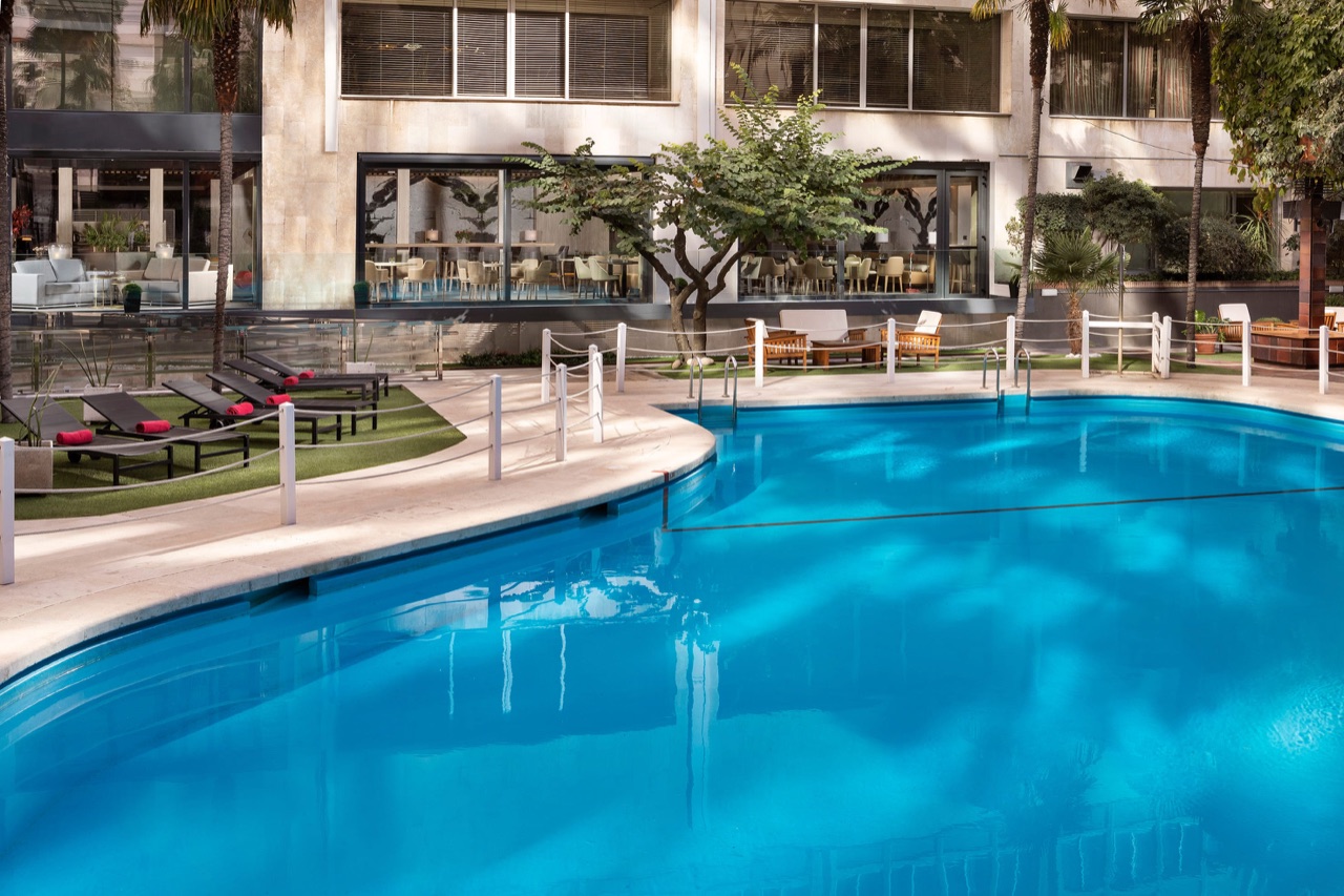Meliá Castilla's outdoor pool surrounded by palm trees, sun loungers and the glass-fronted lobby lounge behind it.