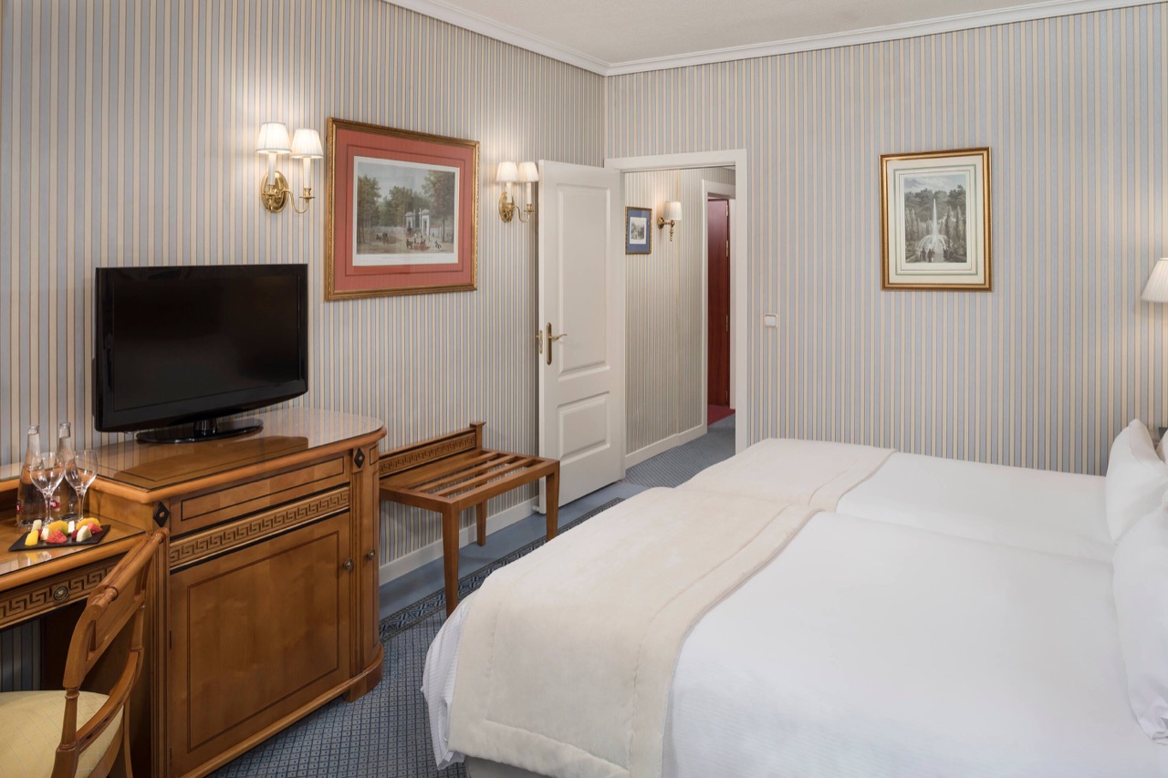 A Classic Room at Meliá Castilla with two beds, striped wallpaper, a wall-mounted TV on a wooden cabinet and framed prints.
