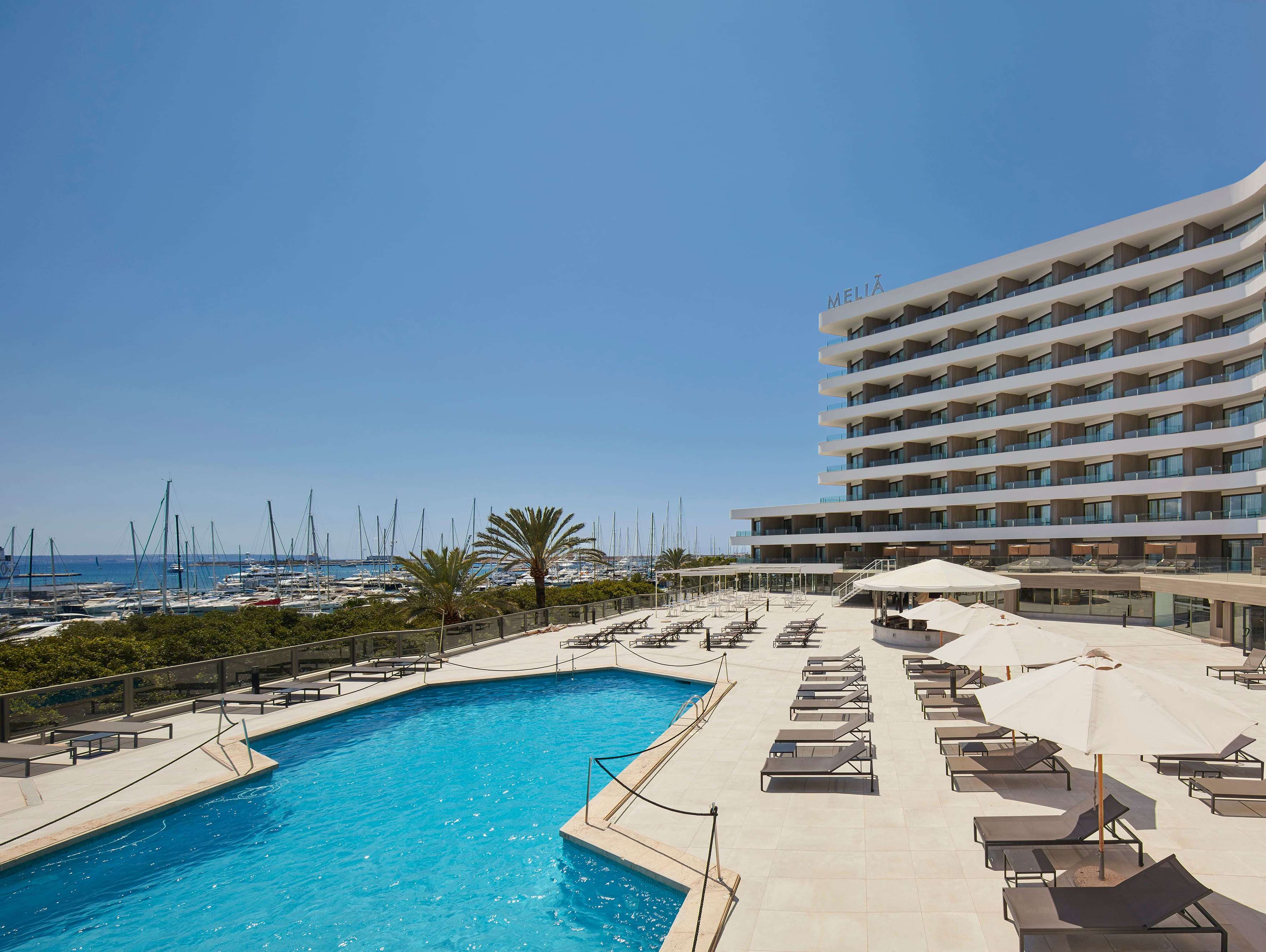 Meliá-branded hotel tower with balconied rooms above an outdoor pool and sun loungers, overlooking the Palma marina's sailboat masts
