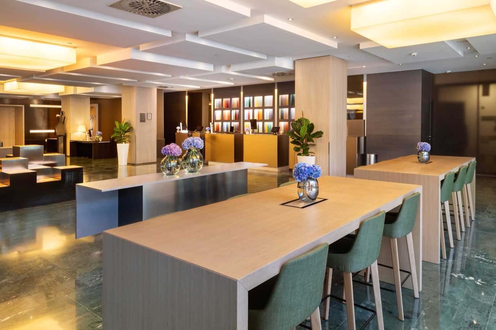 Modern lobby with a reception desk, a colourful art wall and communal wood tables