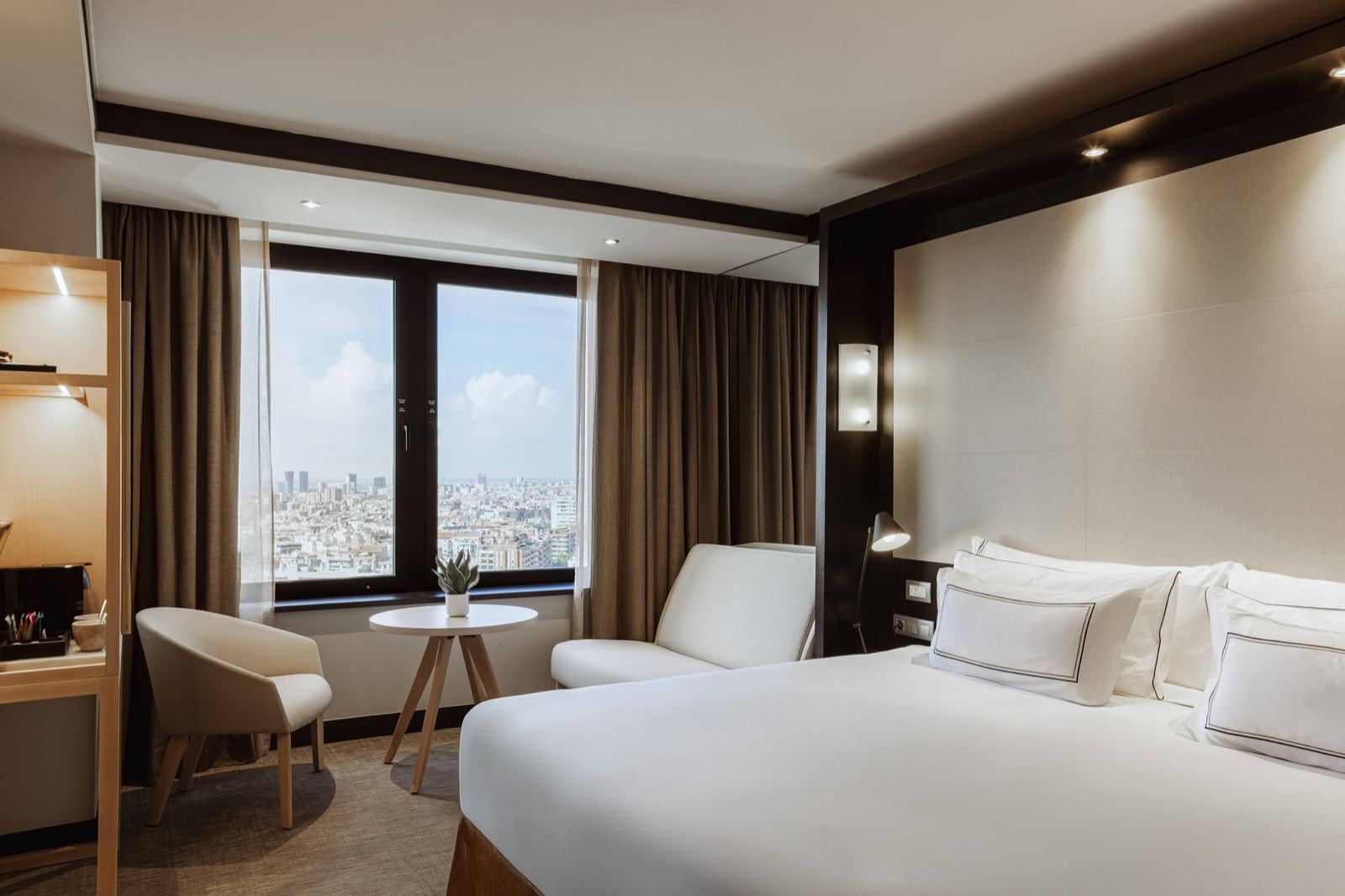 Room with a king bed, an armchair and a window over the Barcelona skyline