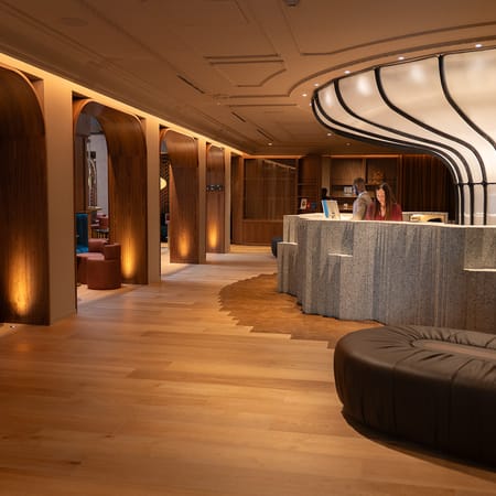The lobby at Mercer Madrid: a curved stone reception desk, timber-clad columns and a wide oak floor.