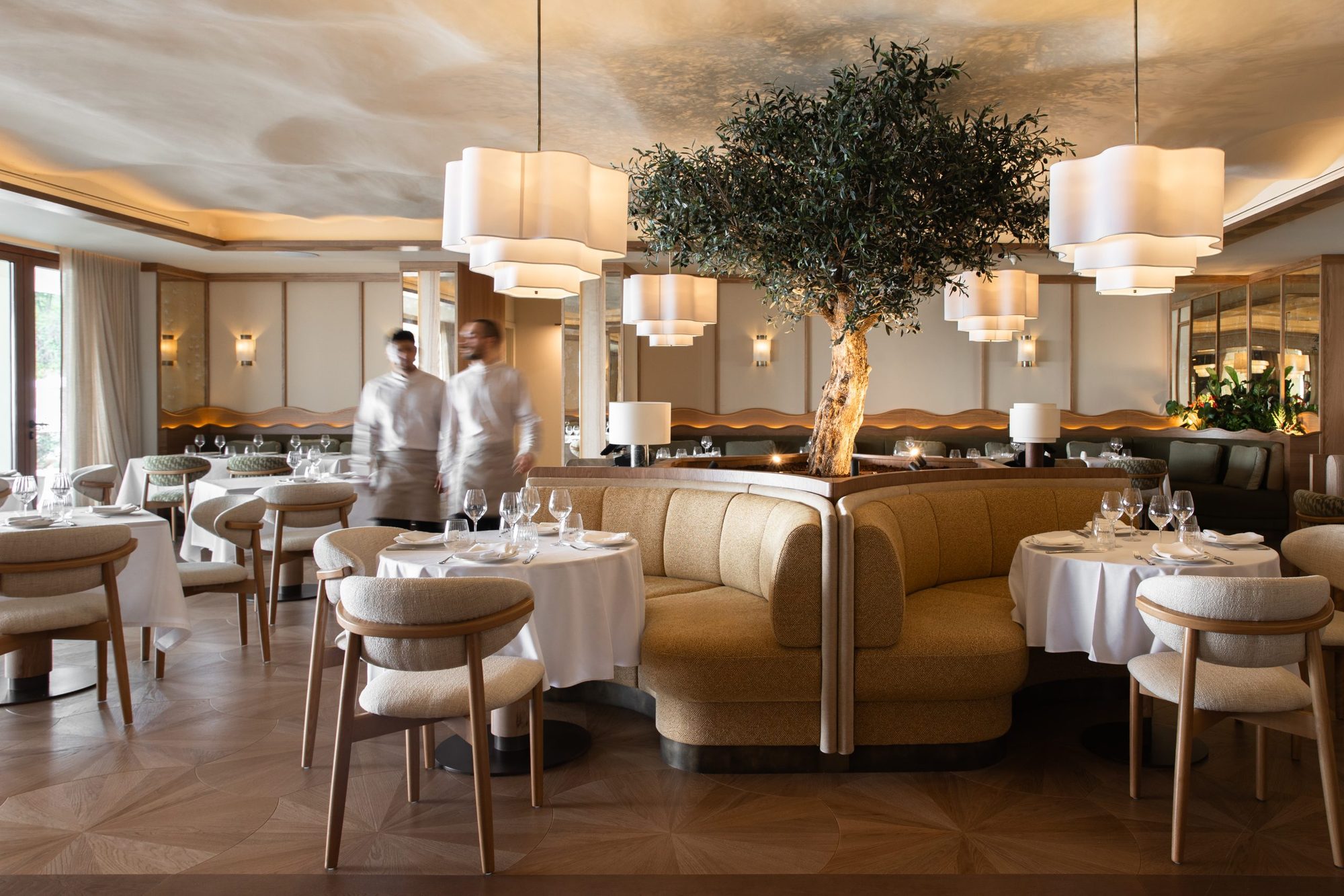 Albarada restaurant at METT Barcelona with a curved banquette wrapped around a live olive tree centerpiece, tiered paper pendant lights, and tables set for service