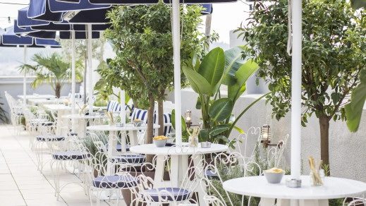 Terrace dining area at Midmost Barcelona with white bistro tables and wire chairs set among potted trees under navy umbrellas