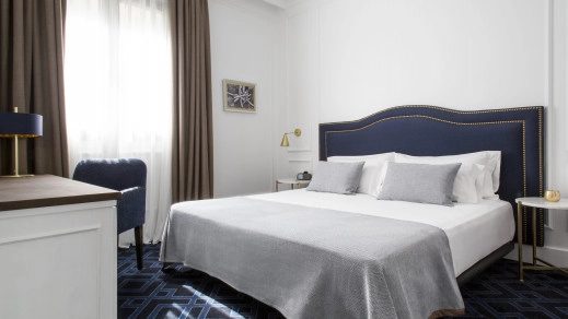 Guest room at Midmost Barcelona with a navy upholstered headboard, grey bedspread, and a patterned carpet in blue tones