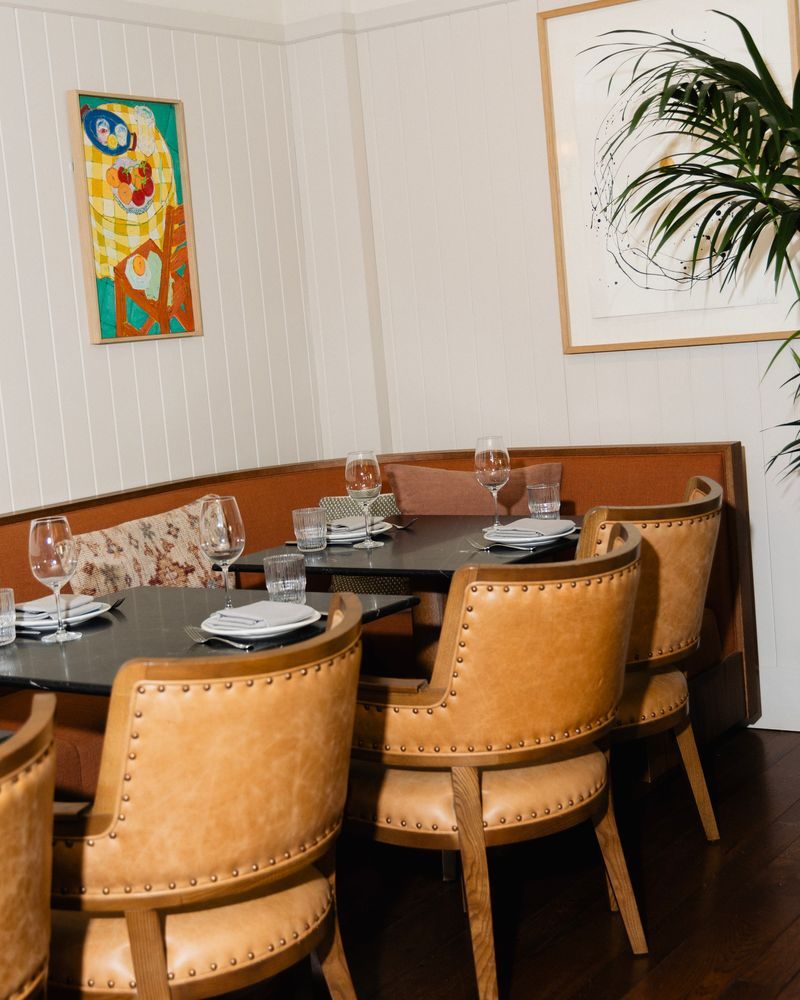 Volta restaurant at Borneta with cognac leather studded chairs at dark wood tables set for dining, and a colourful abstract painting on the wall