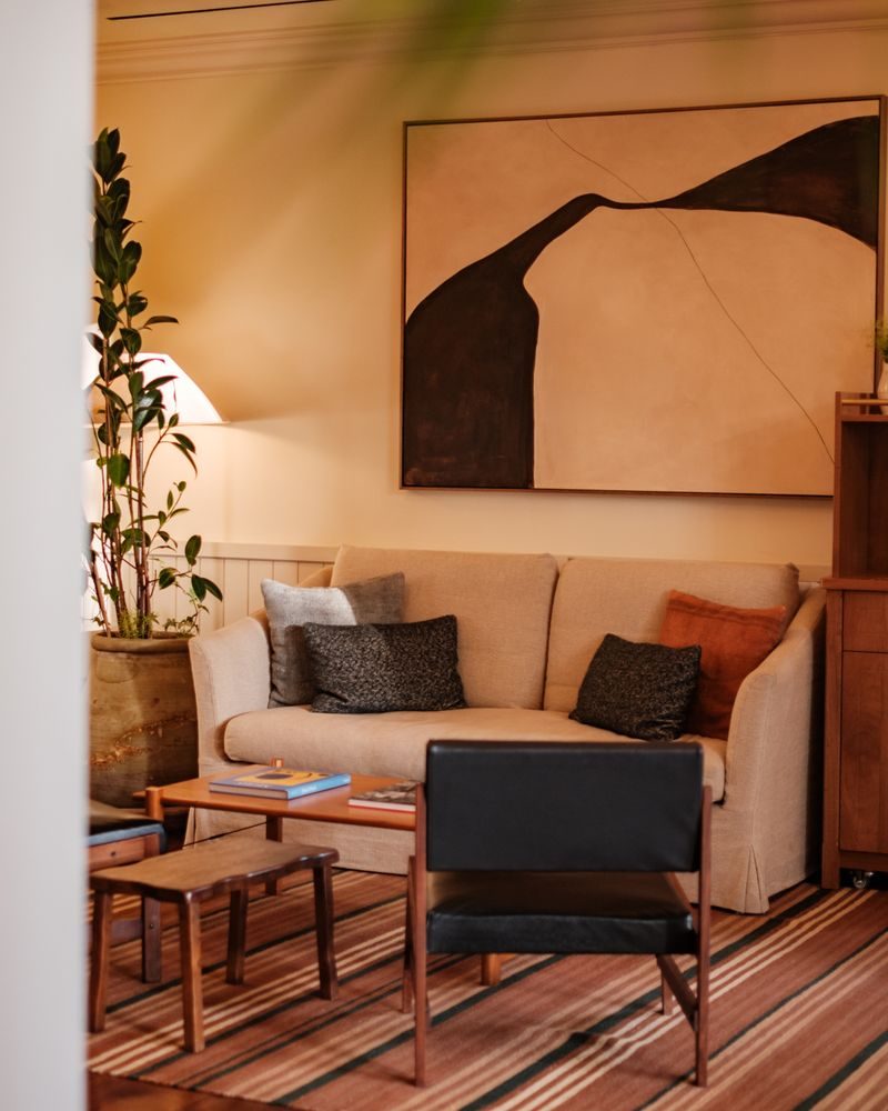 Lounge at Borneta with a cream sofa holding dark and rust cushions, a black leather armchair and a large abstract painting on the wall