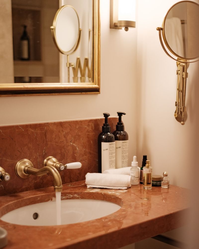 Bathroom vanity at Borneta with a rosso marble counter, brass fittings, a round mirror and amenity bottles beside a folded towel