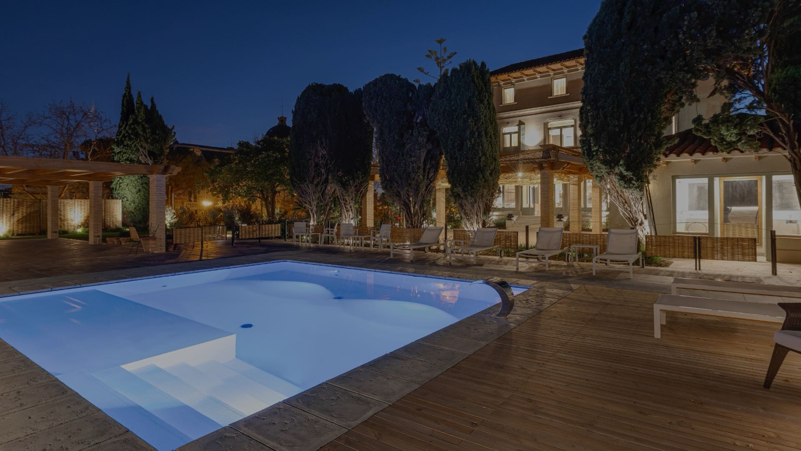 Outdoor pool and garden terrace at night with the villa lit behind