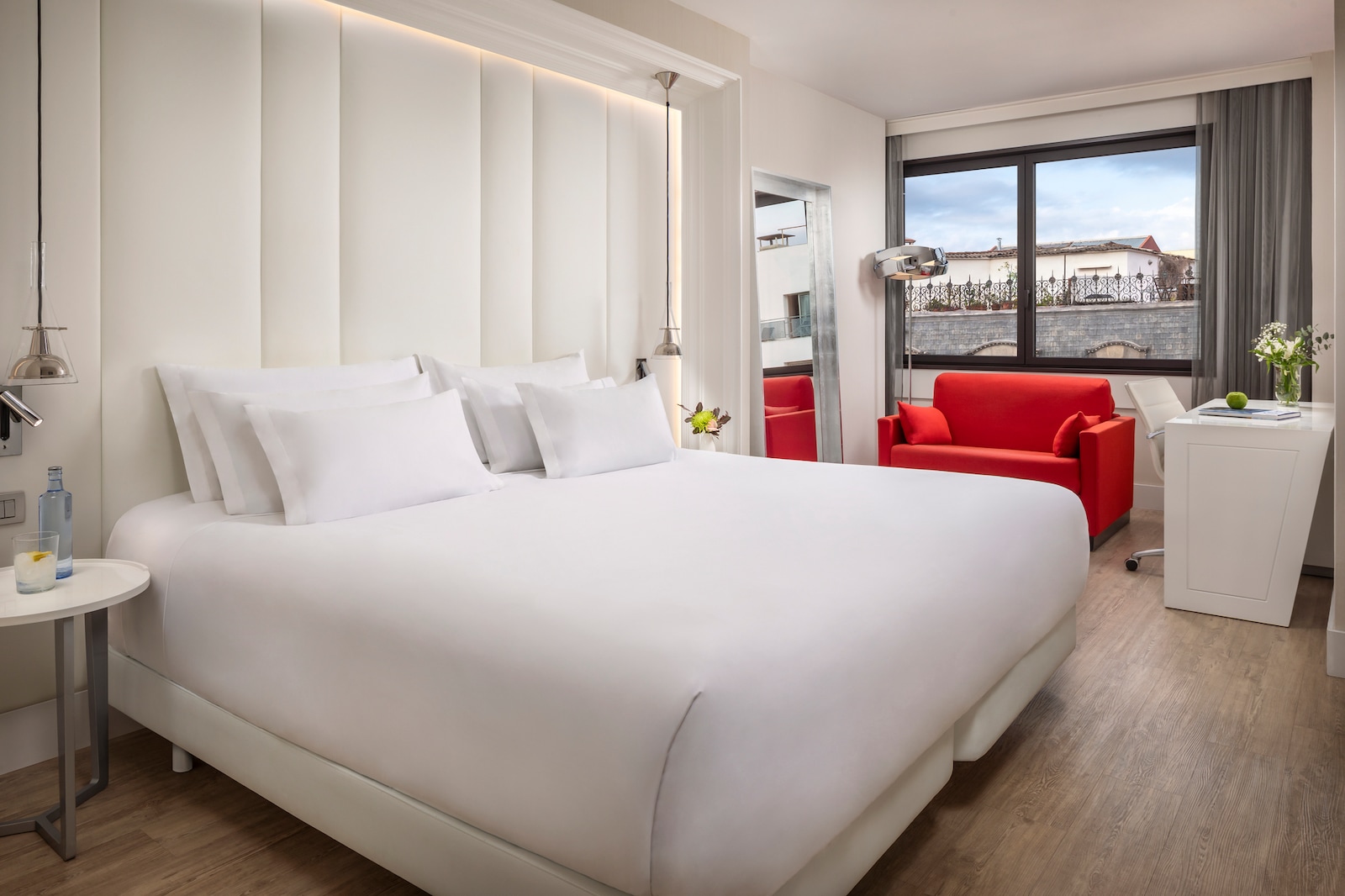 Premium room with a white bed, a red armchair and a city-view window