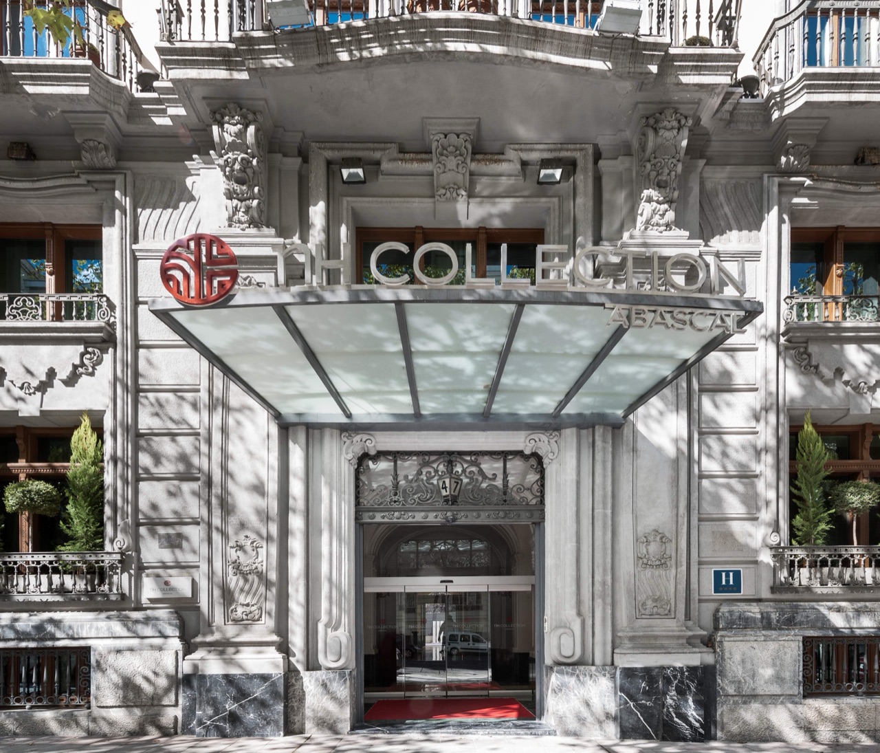 Ornate neoclassical building entrance with a glass canopy, NH COLLECTION ABASCAL signage and the red NH Collection logo above a glass-doored entrance with a red carpet.