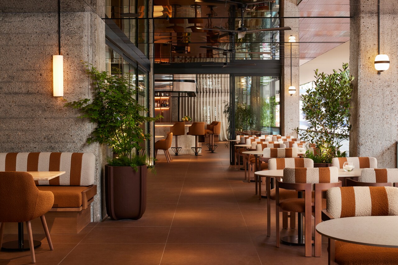 The Bikini Bar terrace and bar area, with striped upholstered chairs, concrete columns and potted plants under pendant lights.