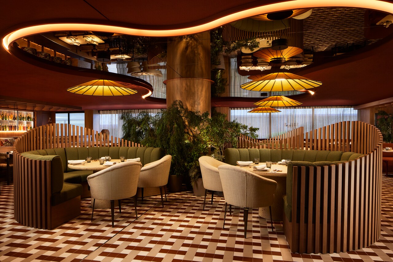 The dining room of Casa de Comidas, with curved wood-slat booths, green upholstered seating and pendant lamps under a mirrored ceiling.