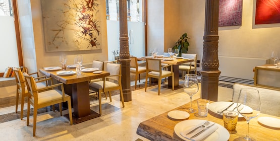 A dining room with white-set tables, pale wooden chairs and slender cast-iron columns beneath large abstract artworks.