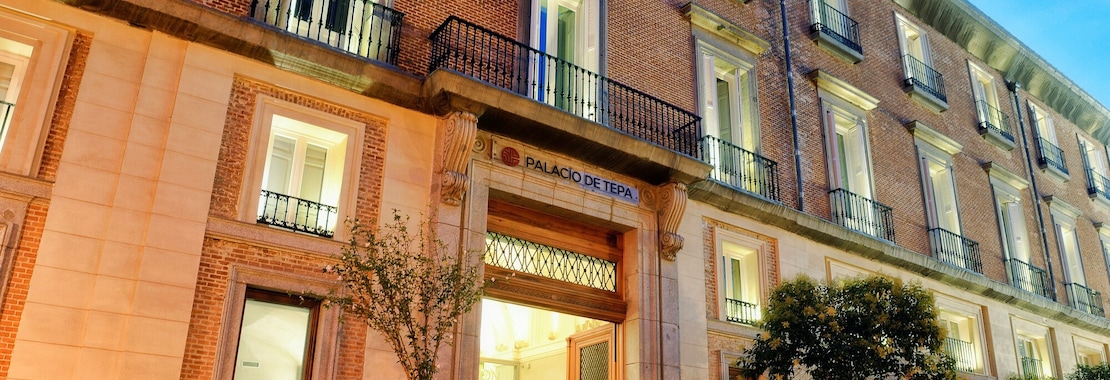 The Palacio de Tepa facade at dusk, brick and stone with wrought-iron balconies above the lit entrance.