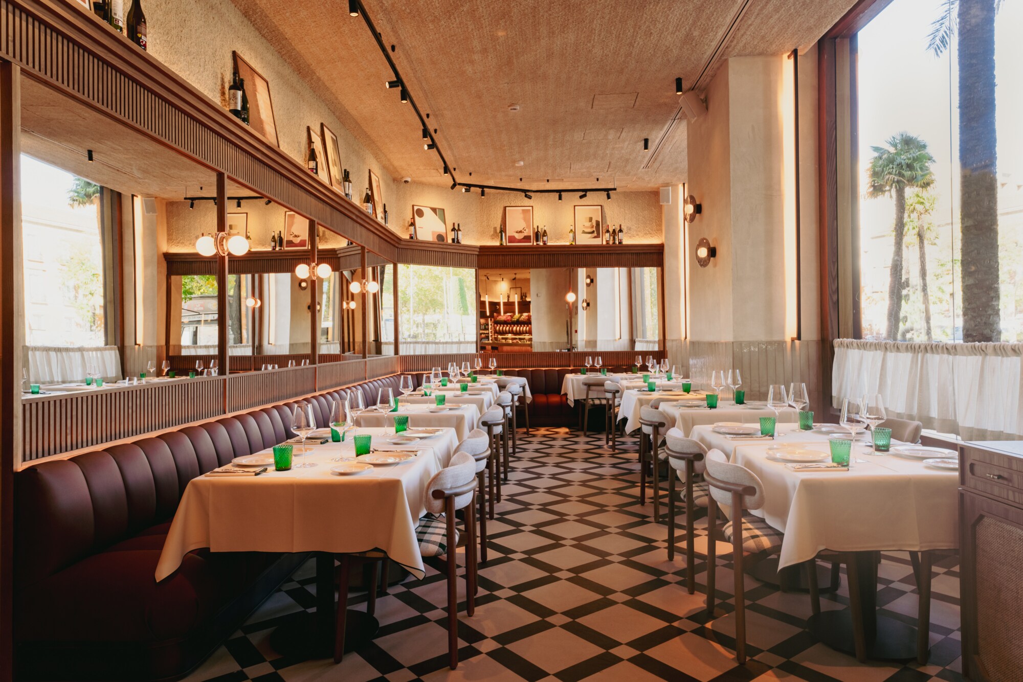 The hotel restaurant's dining room with white-clothed tables set with green glasses, burgundy leather banquettes, mirrored walls, framed prints and a black-and-white checkerboard floor.