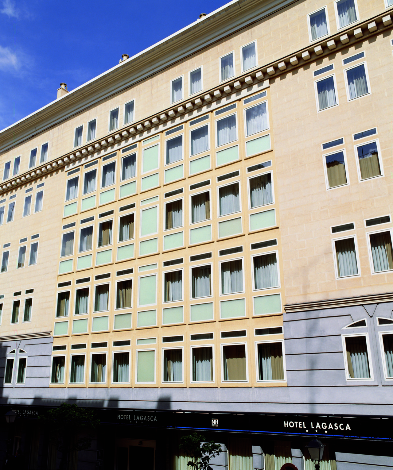 The hotel's pale stone facade on Calle de Lagasca, rows of green-shuttered windows under a blue sky, with the Hotel Lagasca sign over the entrance.