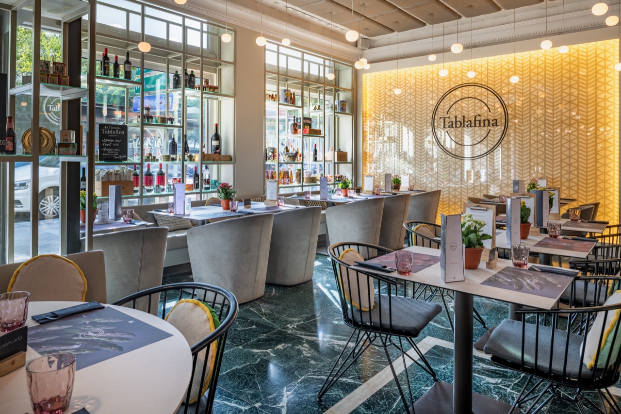 Tablafina dining room with a marble floor, grey upholstered chairs and a mustard patterned feature wall bearing the Tablafina logo.