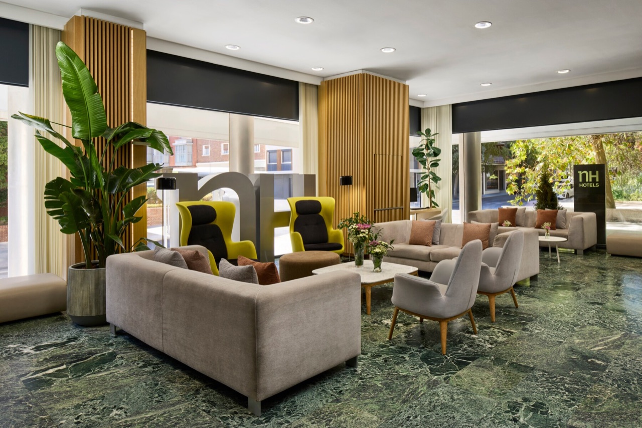 NH Madrid Ventas's lobby lounge with grey sofas, yellow wing chairs, a large potted plant and a green marble floor.