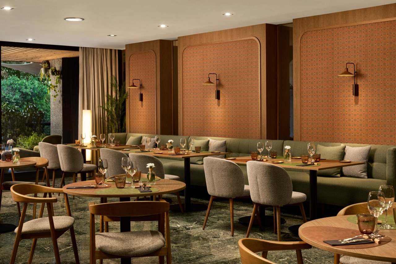 The hotel's restaurant with round wooden tables, green banquette seating and terracotta-tiled wall panels, overlooking the garden.