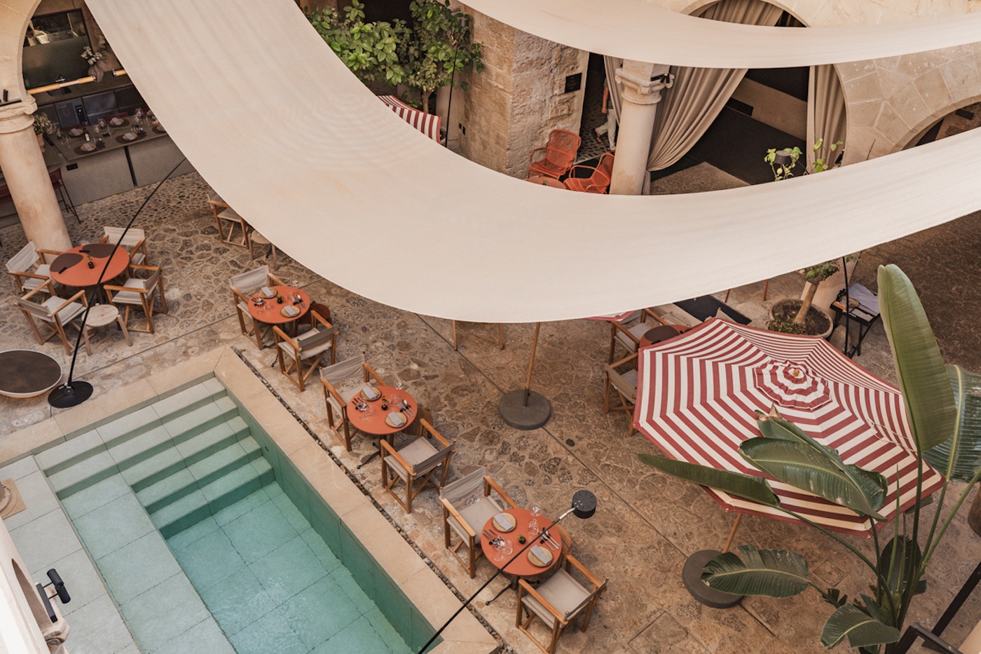 Aerial view of the courtyard pool surrounded by dining tables and a striped umbrella