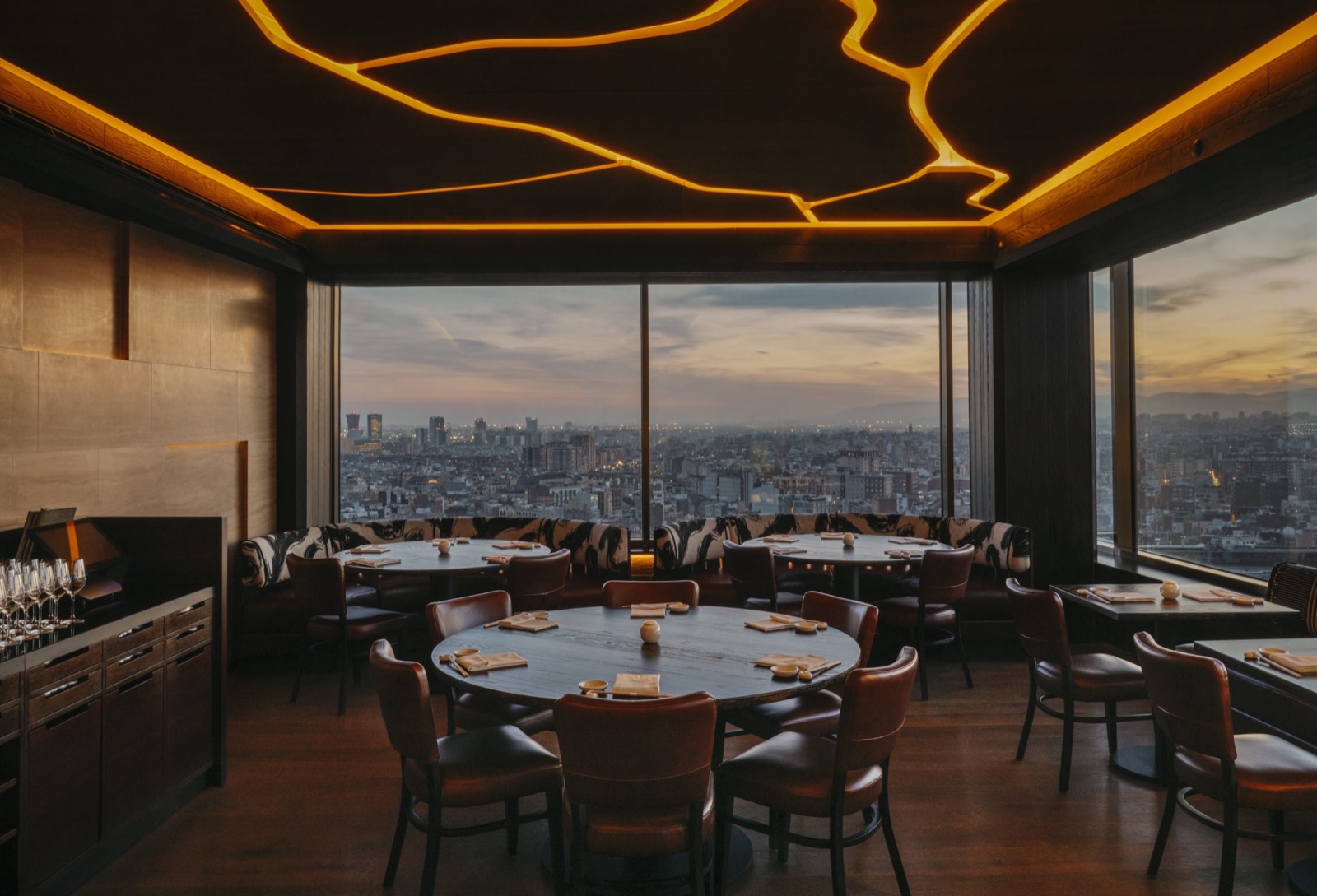 Restaurant dining room with a glowing branch-pattern ceiling and a dusk skyline view